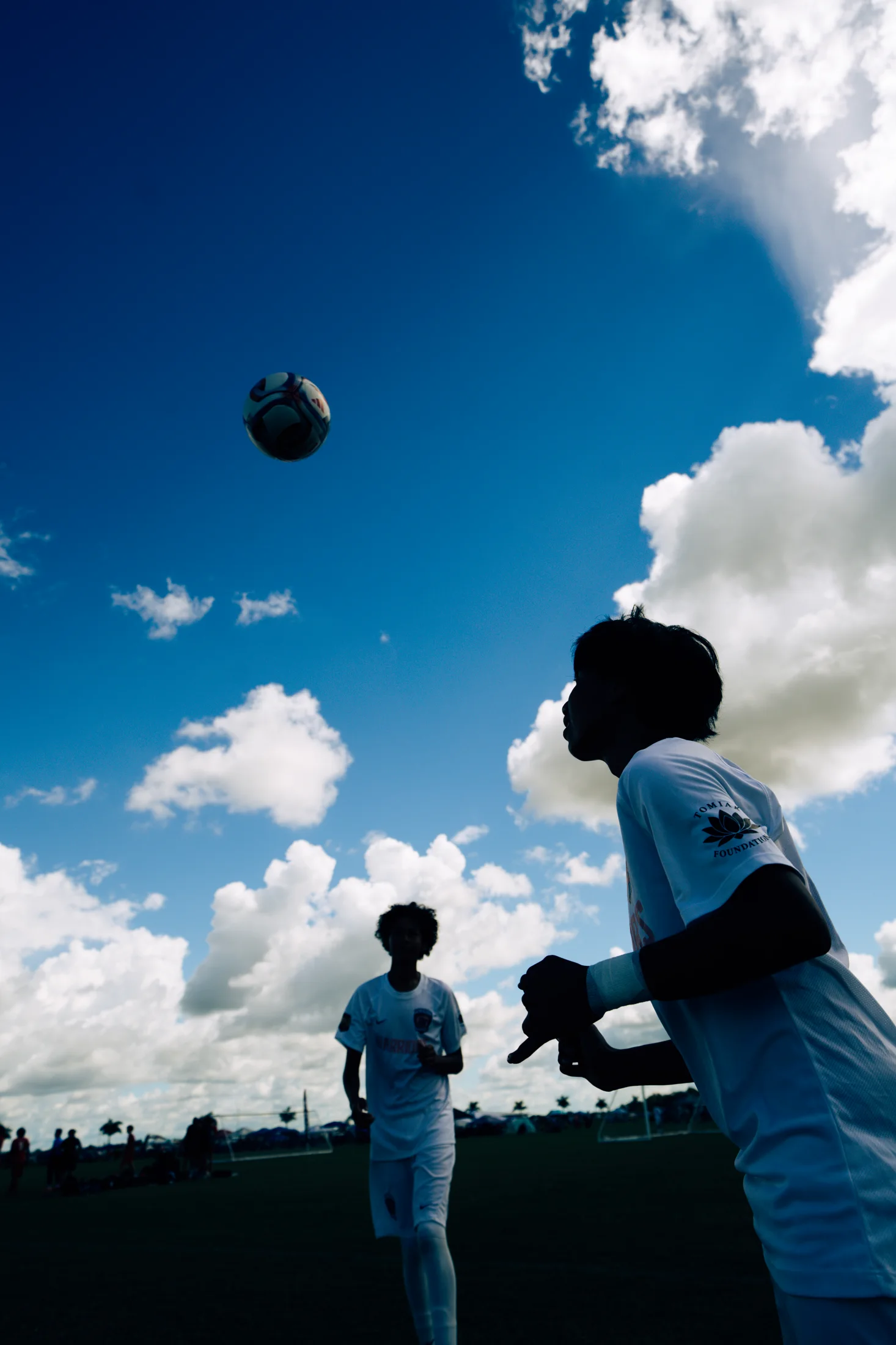 Silhouetted soccer players following the ball beneath clouds