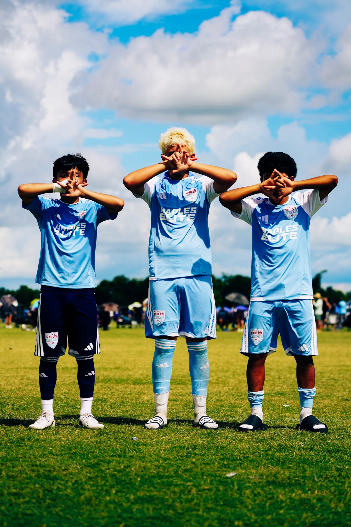 Three soccer players posing together beneath a bright sky